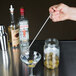 A hand using an American Metalcraft stainless steel bar ejector fork to place an olive in a martini glass.