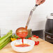 A person using a Vollrath Jacob's Pride ladle with a black Kool Touch handle to pour tomato sauce into a bowl.
