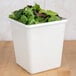A white square melamine crock with green leaves in it.
