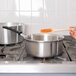 A person stirring sauce in a Vollrath stainless steel sauce pan on a stove.