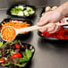 A person using a Carlisle long handle solid portion spoon to serve shredded carrots and vegetables into a salad bowl.