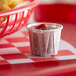A small cup of ketchup in a red and white checkered basket with fries on a tray.