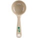 A Carlisle beige measuring spoon with a green handle.