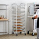 A man standing in a kitchen with a Regency sheet pan rack holding trays of food.