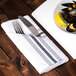 A Snap Drape black and white striped Softweave cloth napkin with a knife and fork on it next to a plate of mussels and a lemon.