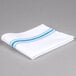 A folded white Snap Drape cloth napkin with blue stripes.