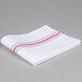 A folded white Snap Drape cloth napkin with red stripes.