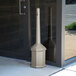 A beige Commercial Zone Smokers' Outpost cigarette receptacle next to a glass door.