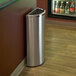 A stainless steel Commercial Zone Precision half round trash receptacle next to a wall.