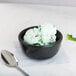A bowl of mint chocolate chip ice cream on a table with a spoon.
