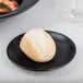 A round white bread roll on a black Hall China Foundry coupe plate.