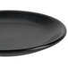 A close-up of a Hall China Foundry black coupe plate with a rim.