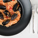A Hall China black Mediterranean pasta bowl filled with spaghetti, mussels, and sauce.