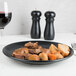 A Hall China Foundry black coupe plate with meat and vegetables on a table.