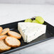 A Hall China black rectangular platter with blue cheese and grapes on it.