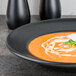 A black Hall China Mediterranean rim soup bowl with cream and basil soup in it.