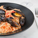 A black Hall China bowl filled with spaghetti, mussels and clams.
