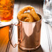 A Libbey copper Moscow mule mug filled with fried onion rings on a table.