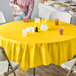 A table with bowls of food covered by a yellow round Creative Converting School Bus Yellow OctyRound tablecloth.