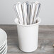 A white cup with a Cal-Mil white solid melamine flatware cylinder full of silverware.
