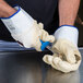A person wearing Cordova Ruffian rubber gloves with a blue handle using a knife to cut up oysters.