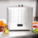 A stainless steel Avantco food dehydrator with a removable door on a counter with bowls of fruit and vegetables.