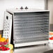 An Avantco stainless steel food dehydrator with trays of fruit on the counter.