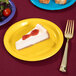 A piece of cheesecake on a Creative Converting School Bus Yellow paper plate next to a fork.