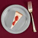 A piece of cheesecake with strawberry jam on a Creative Converting shimmering silver paper plate.