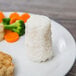 A plate of white rice with carrots, broccoli, and fried chicken on the side, served on a wood table.