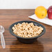 A Dart black laminated foam bowl filled with cereal, apples, and oranges on a table.