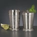 A Libbey stainless steel mint julep cup filled with ice and mint leaves next to a lime wedge.