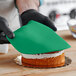 A person wearing black gloves uses Satin Ice Green Vanilla Rolled Fondant to cover a cake.