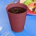 A burgundy Creative Converting plastic cup full of liquid on a table with a blue surface.