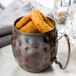 A World Tableware Hammered Antique Copper Moscow Mule Mug filled with fried food.