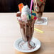 Two Anchor Hocking soda glasses filled with chocolate milk and candy with whipped cream on top.