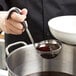 A person using a Vollrath stainless steel ladle with a black Kool-Touch handle to serve liquid into a bowl.