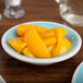 A close up of a Carlisle Aqua Melamine Fruit Bowl filled with yellow fruit on a table.