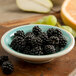 A Carlisle Aqua Melamine fruit bowl filled with blackberries on a wooden surface.