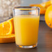 A close up of a Carlisle clear Tritan plastic juice glass filled with orange juice and a slice of orange.