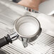 A person pouring Urnex Cafiza espresso machine cleaning powder into a coffee machine.