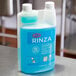 A blue bottle of Urnex Rinza milk frother cleaner on a counter.