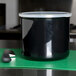 A black Carlisle crock with a white lid and a knife on a green cutting board.