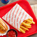 A red tray of Carnival King extra large French fry bags with a hot dog and fries on it.
