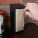 A hand putting a Choice Kraft Natural Tall-Fold Dispenser Napkin in a dispenser.