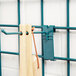 A green metal Metro SmartWall G3 hook holding a wooden spoon over a pair of wooden spoons on a metal rack.