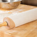 A cotton Ateco rolling pin cover on a rolling pin over a wooden surface.