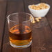 A Spiegelau whiskey glass filled with brown liquid next to a bowl of peanuts.