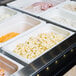 A white Cambro 1/3 size food pan filled with food on a buffet counter.
