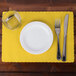 A white plate with a fork and knife on a yellow Hoffmaster scalloped paper placemat.